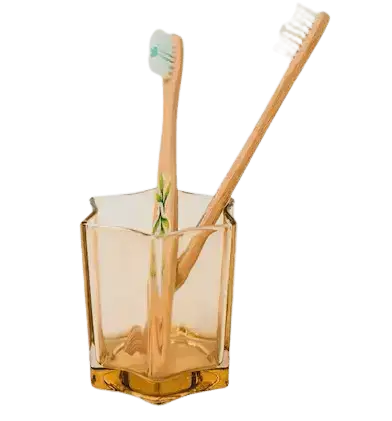 Two bamboo toothbrushes stand upright in a translucent, amber-colored glass holder.