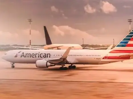 An American Airlines plane is parked on the tarmac at an airport, under a partly cloudy sky.
